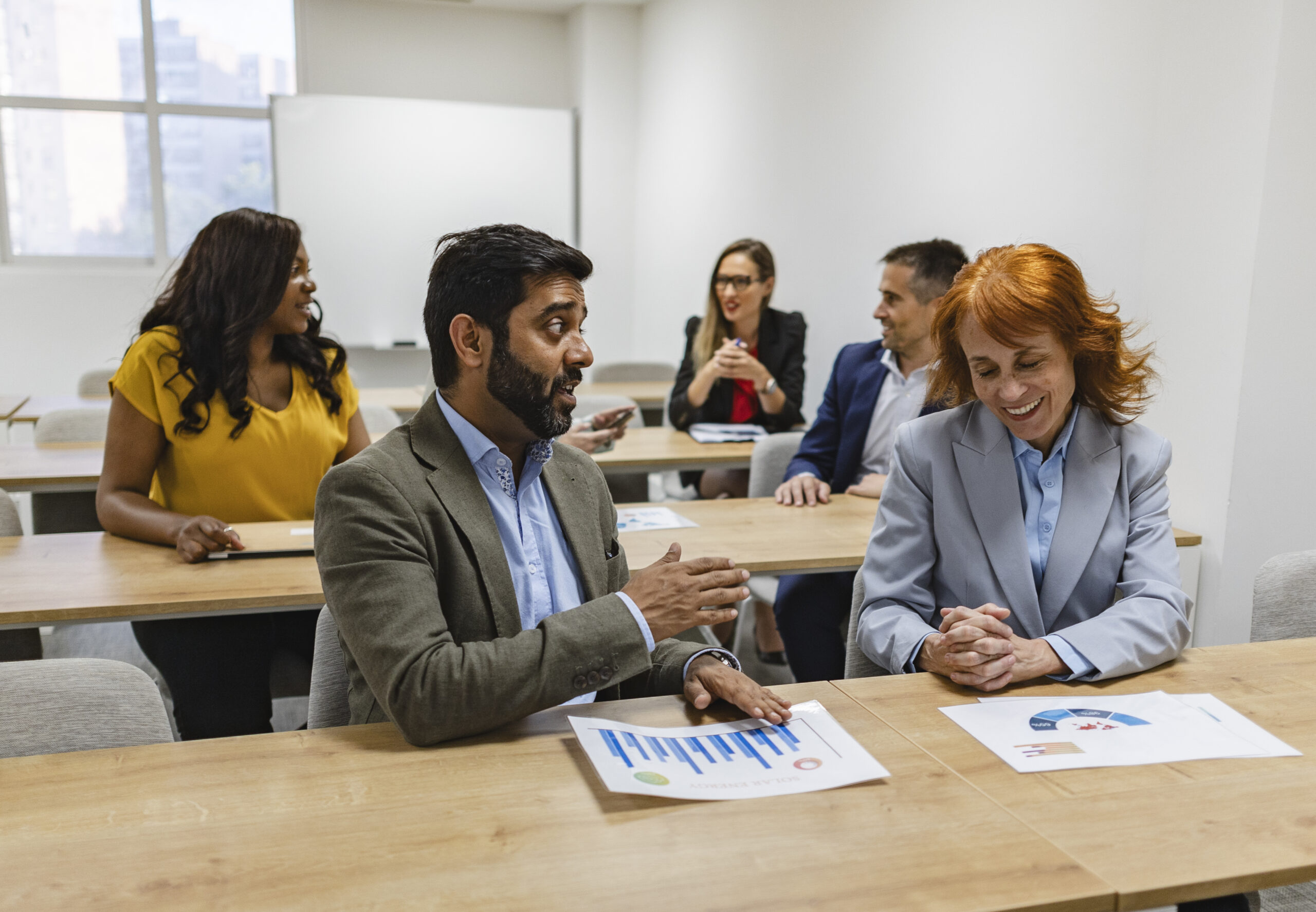 Diverse business team seated in a workshop setting, exchanging ideas and reviewing documents in a relaxed environment.